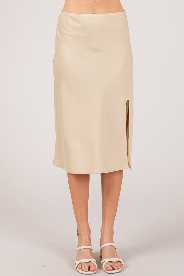 Woman wearing a satin midi skirt with a side slit in a cream tone, paired with a fitted black top for an elegant, polished look.