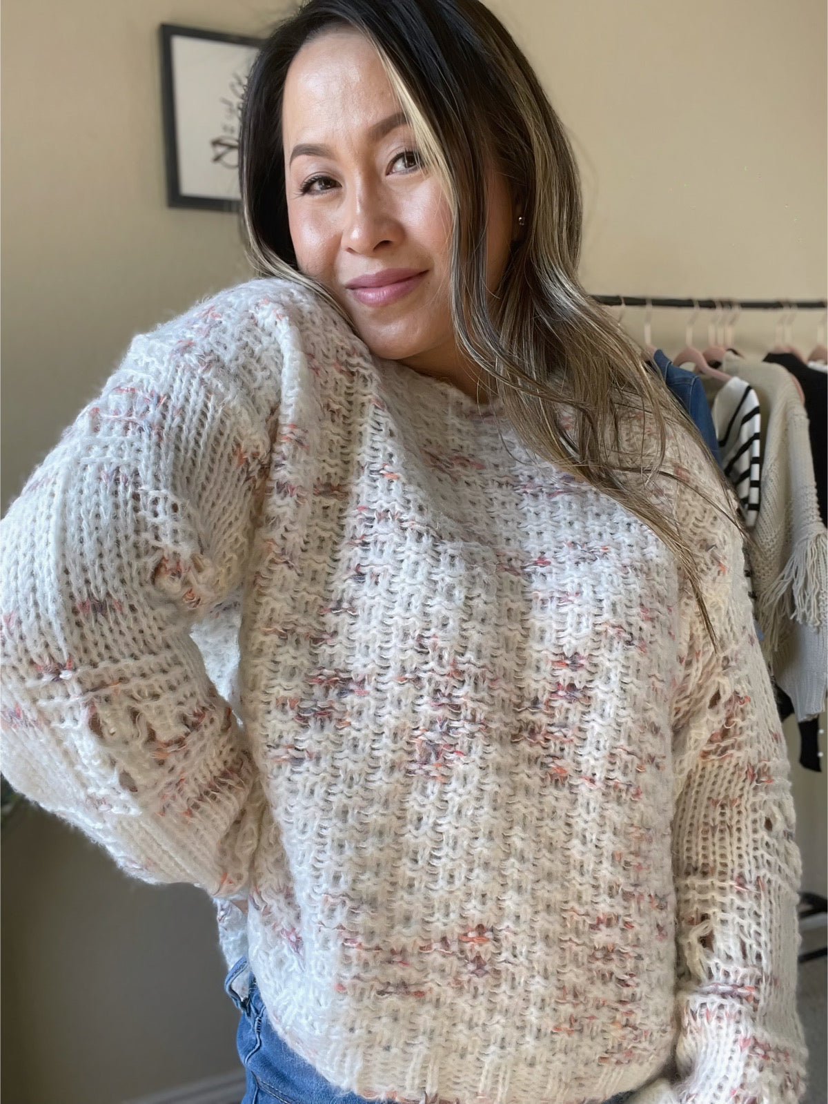 Woman wearing a speckled knit sweater in pink and cream tones, paired with distressed jeans for a casual and stylish outfit.