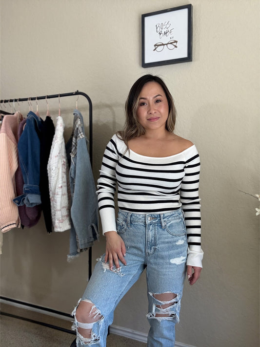 Front view of a model  black and white striped off-shoulder sweater with a classic knit design.