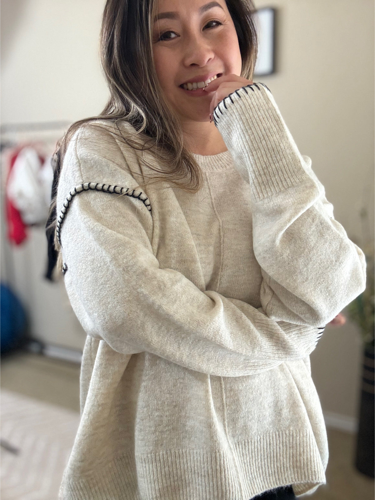 Woman wearing a cozy knit pullover sweater in a soft cream color with black stitched detailing on the sleeves, styled with ripped jeans