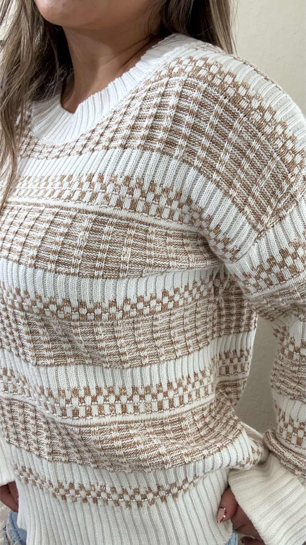 Woman wearing a cream and tan textured knit sweater with a woven pattern, styled with distressed jeans for a casual and stylish look.