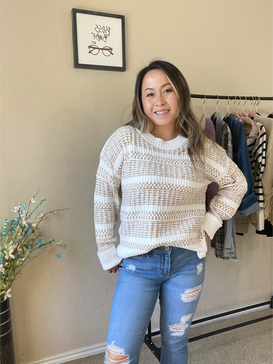 Woman wearing a cream and tan textured knit sweater with a woven pattern, styled with distressed jeans for a casual and stylish look.