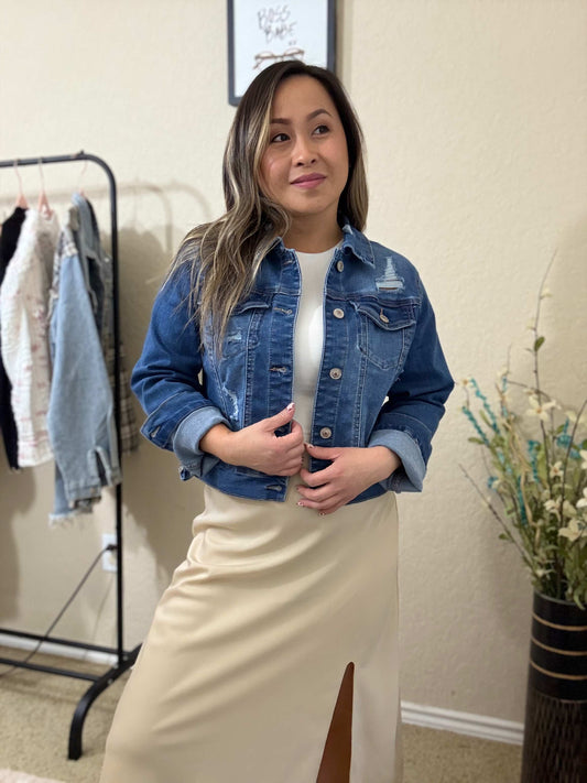 Front view of woman wearing a blue destructed denim jacket featuring distressed details and button-down styling.