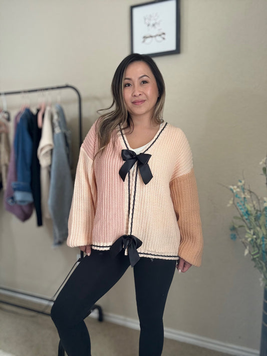 Front view of a woman wearing a pink and tan colorblock knit cardigan with black trim and an open-front design.