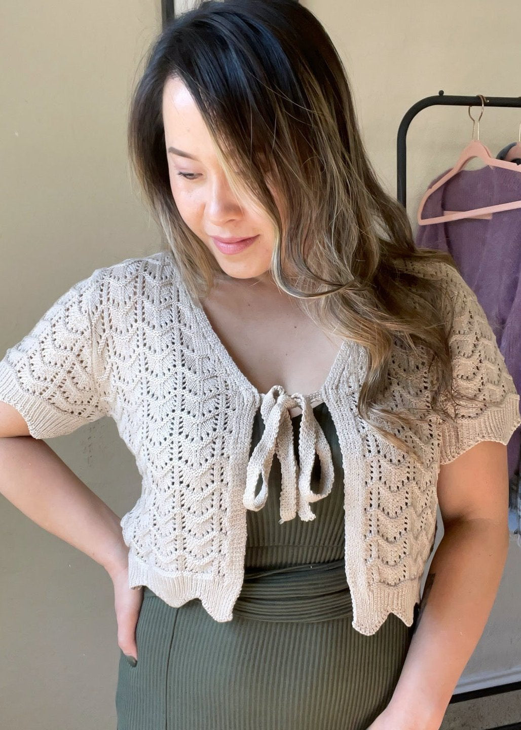 Front view of a woman wearing a beige crochet knit tie-front cropped cardigan with short sleeves, scalloped hem, and delicate detailing.