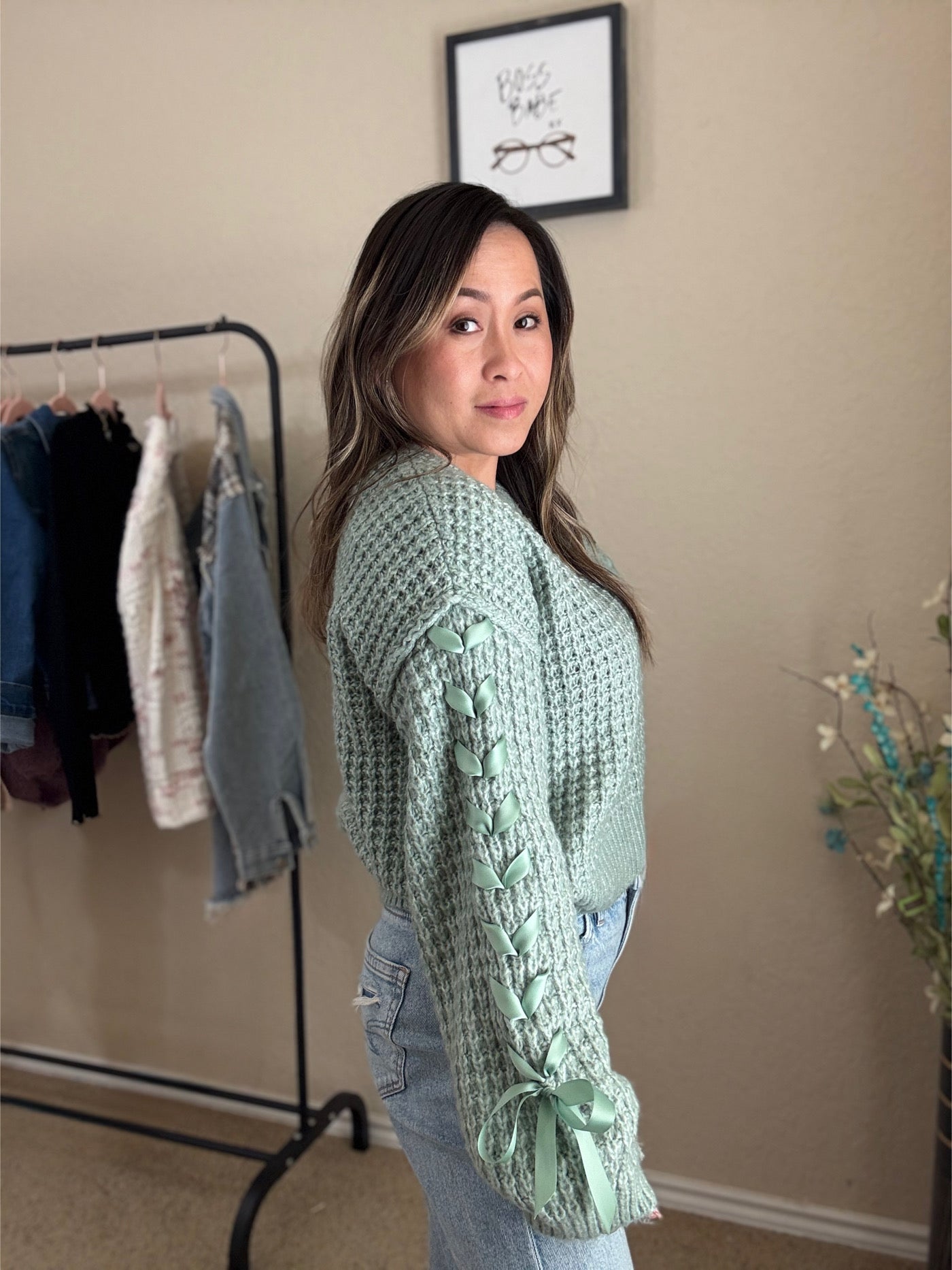 Woman wearing a mint knit sweater with lace-up sleeves and bow details at the cuffs.