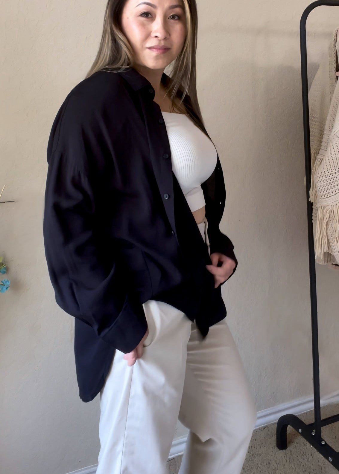 Side view of a woman wearing a black oversized button-down shirt featuring a relaxed fit and lightweight fabric.