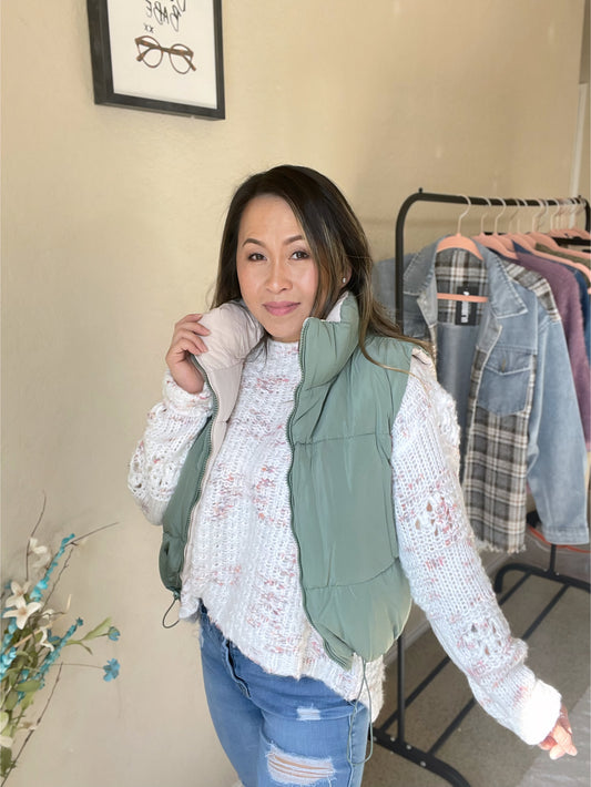 Woman wearing a reversible woven vest paired with a sweater and ripped jeans, styled with casual elegance.