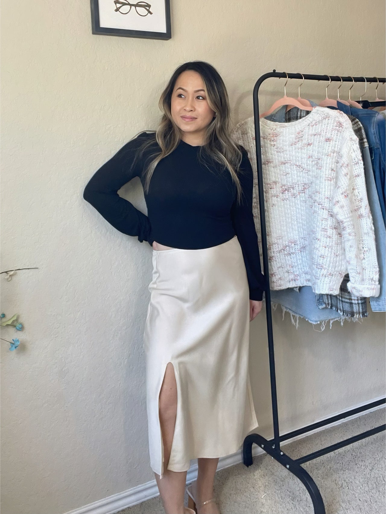 Woman wearing a satin midi skirt with a side slit in a cream tone, paired with a fitted black top for an elegant, polished look.