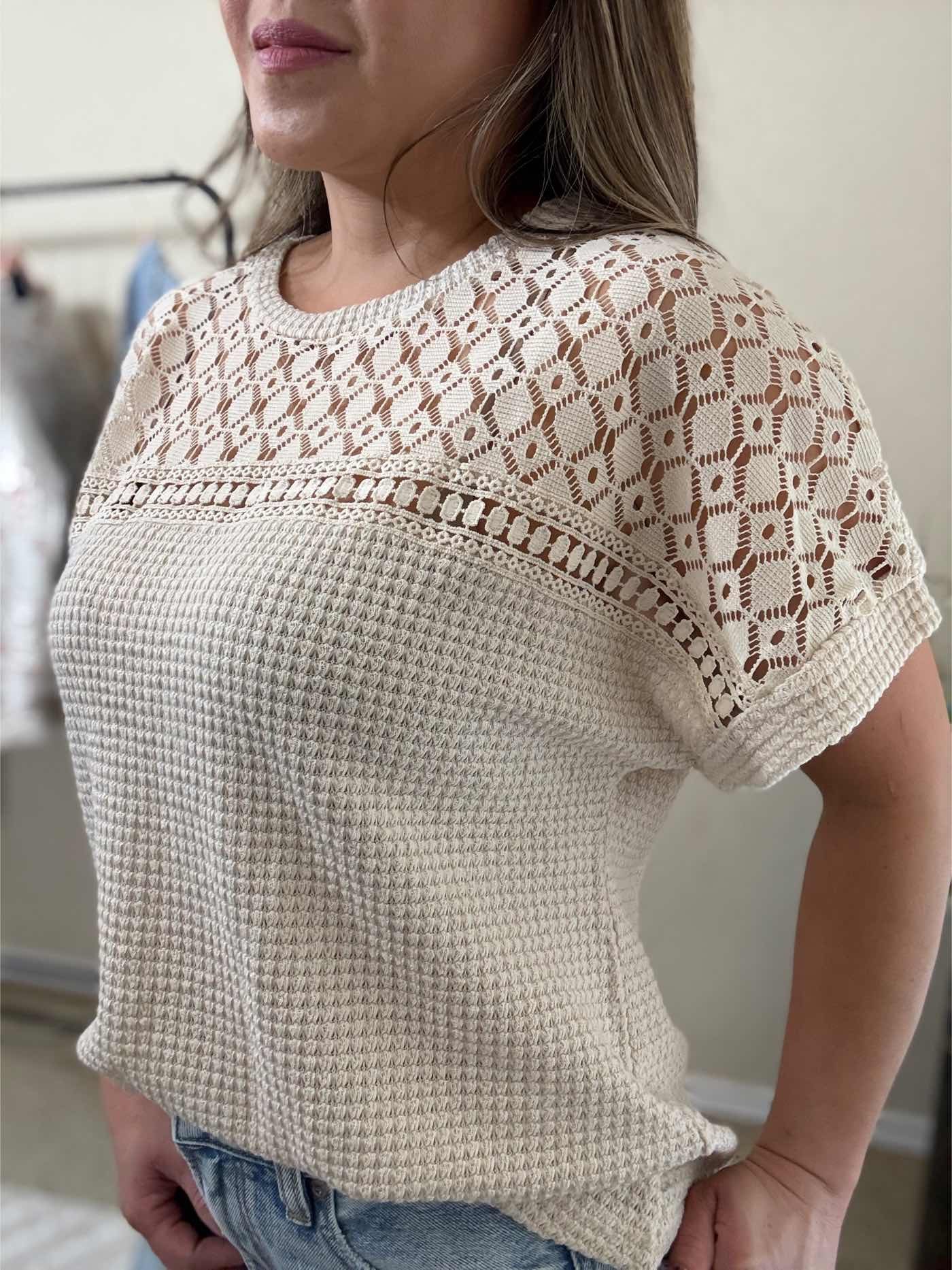 Close up side  view of a woman wearing a beige lace yoke textured top with intricate lace detailing on the yoke and sleeves and a relaxed fit.